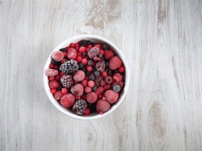 frozen berries, black currant, red currant, raspberry, blueberry. top view in a vintage ceramic white bowl on rustic wooden table isolated